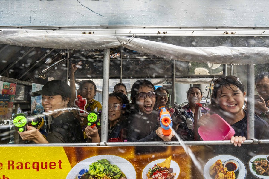 People in the back of a truck playfully shoot water guns toward the photographer.