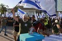 An Israeli military reservist waves a national flag as he drops in a box a signed declaration announcing the suspension of his voluntary reserve duty, in protest of the government's judicial-overhaul bill, in Tel Aviv.