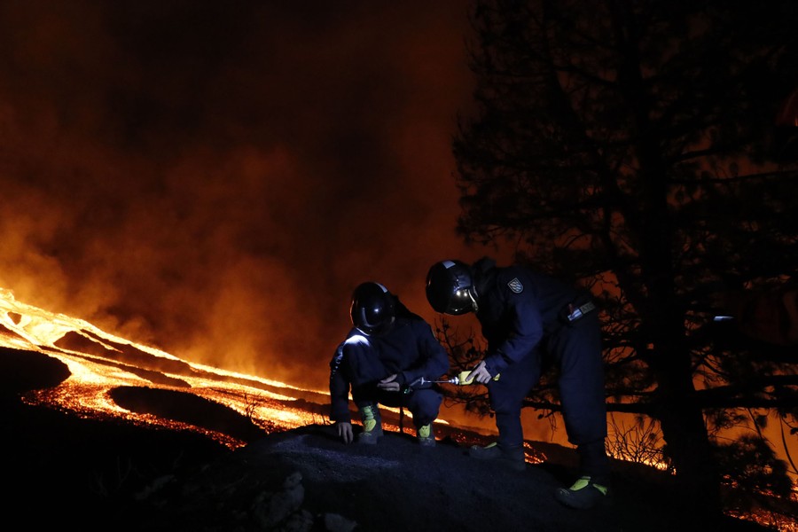 Two people take measurements near a lava flow at night.