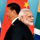 Xi Jinping and Narendra Modi stand next to each other but face in opposite directions in front of flags.