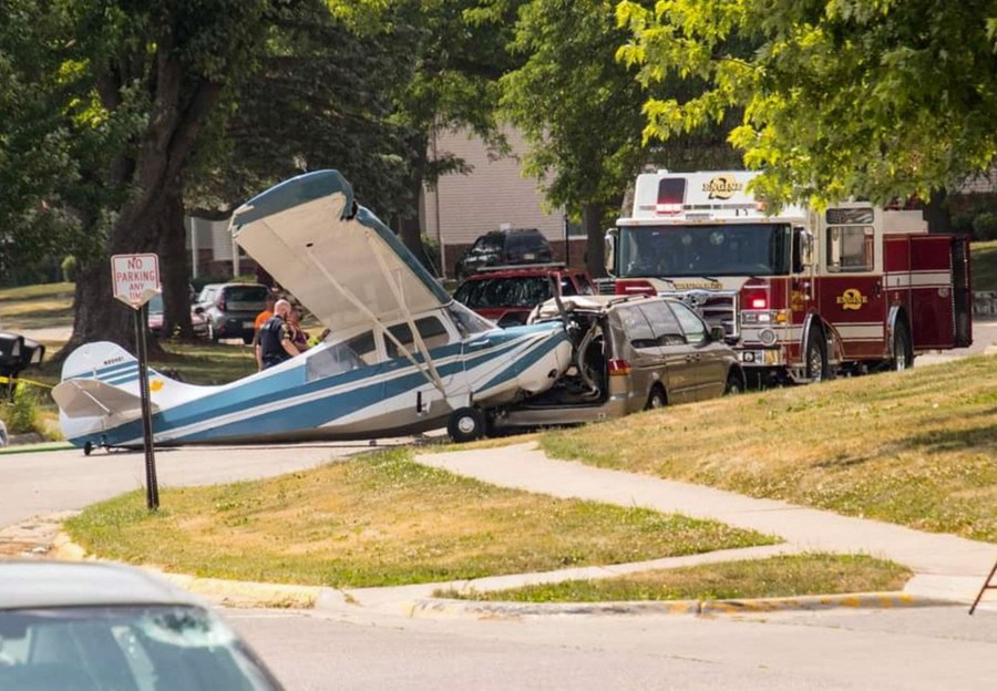A small airplane sits in a residential street, having crashed into the back of a minivan.