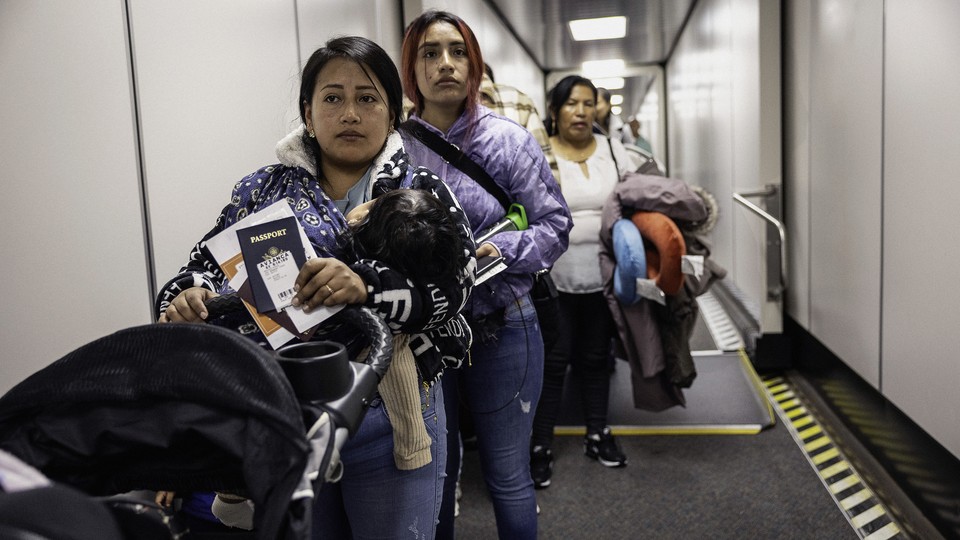 Three women, one holding a baby in her arms and pushing a stroller, stand in line awaiting to board a flight