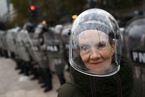 A woman wearing a protective helmet poses in front of a line of riot police during a protest.