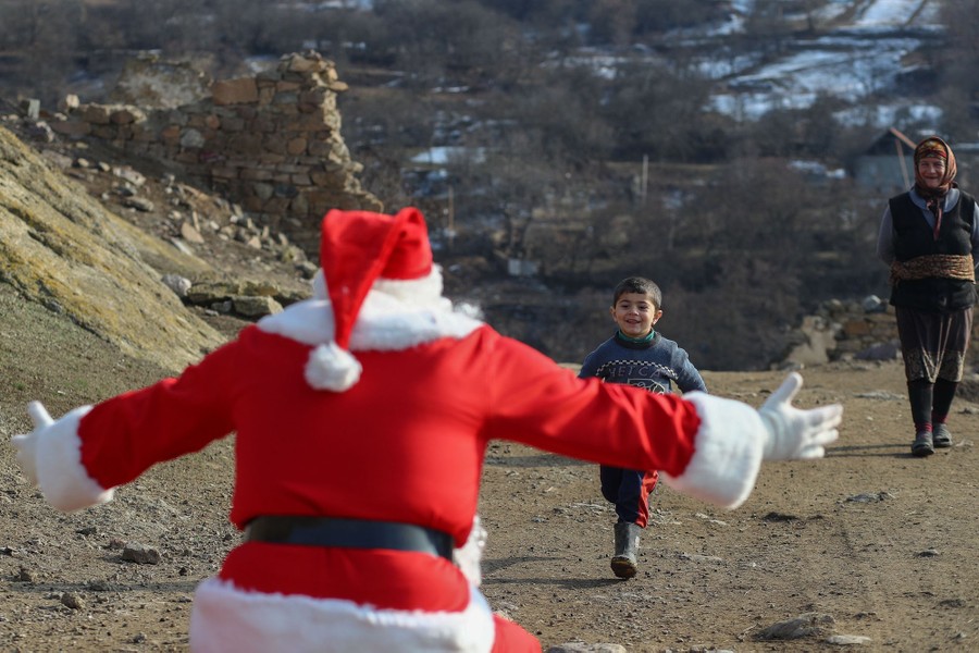 A man dressed as Santa Claus reaches out his arms to greet a running child.