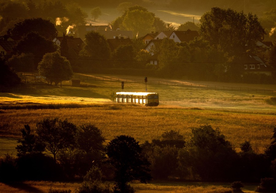 A passenger-train car moves along a track through a field near a city.