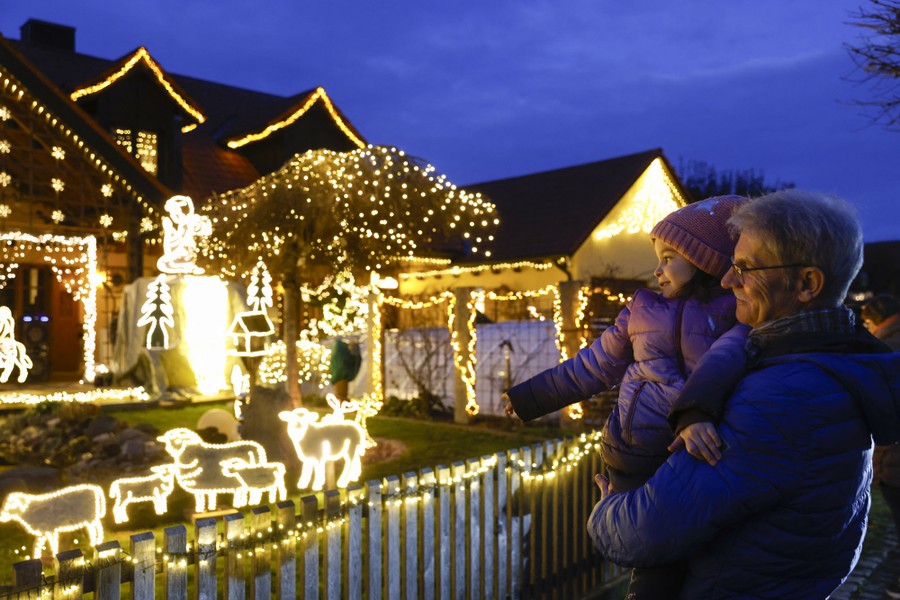 A person holds a child up as they both look at a house covered in many bright Christmas decorations.