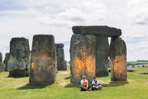 A photo of two protesters sitting in front of Stonehenge, which has orange spray paint on it