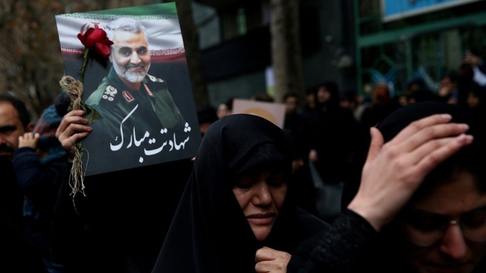 A protester in the middle of a crowd in Iran holds a rose and a photograph of Qassem Soleimani.