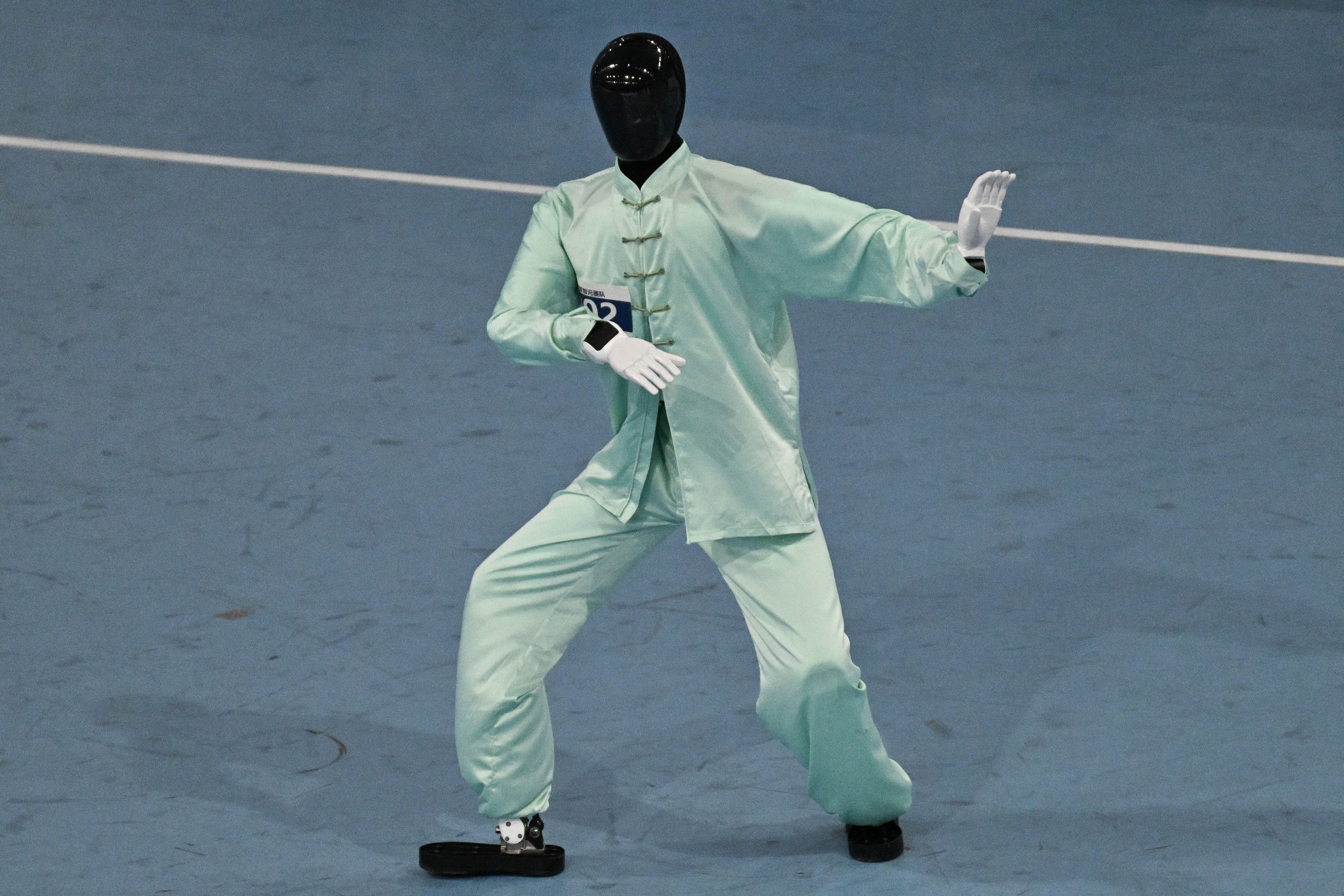 A humanoid robot wearing a tai chi uniform competes in a tai chi event.