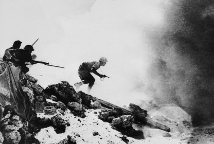 Armed soldiers cautiously advance into a smoke covered battlefield