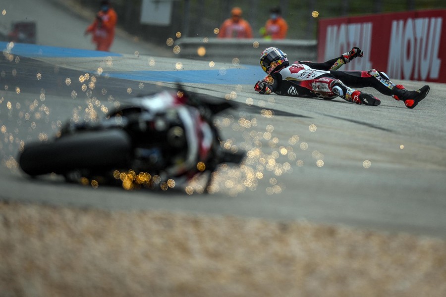 A motorcycle rider slides down a track as his bike scrapes along ahead of him, throwing sparks.