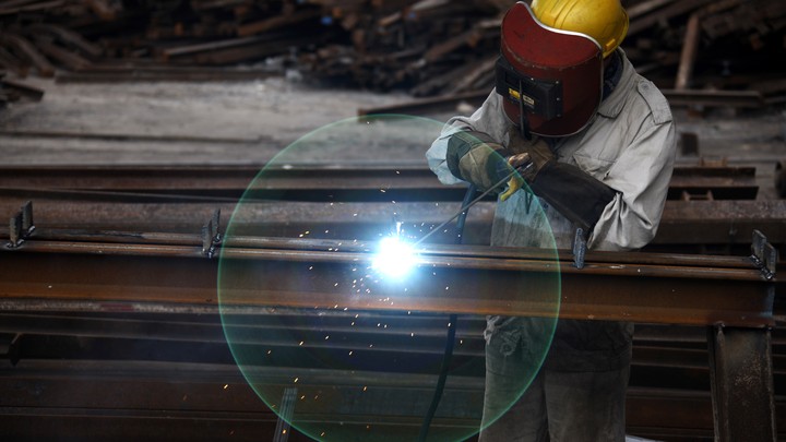 Someone works in a factory. The worker's face is covered with a protective helmet. A flash of light flickers.