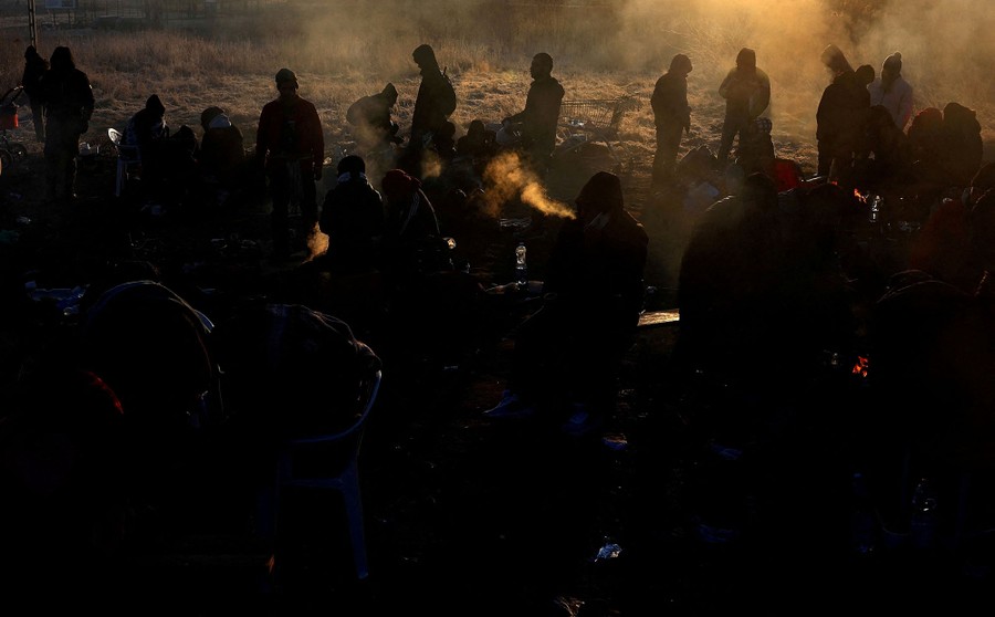 Dozens of people mill about in a field on a cold day, their breath visible in the air.