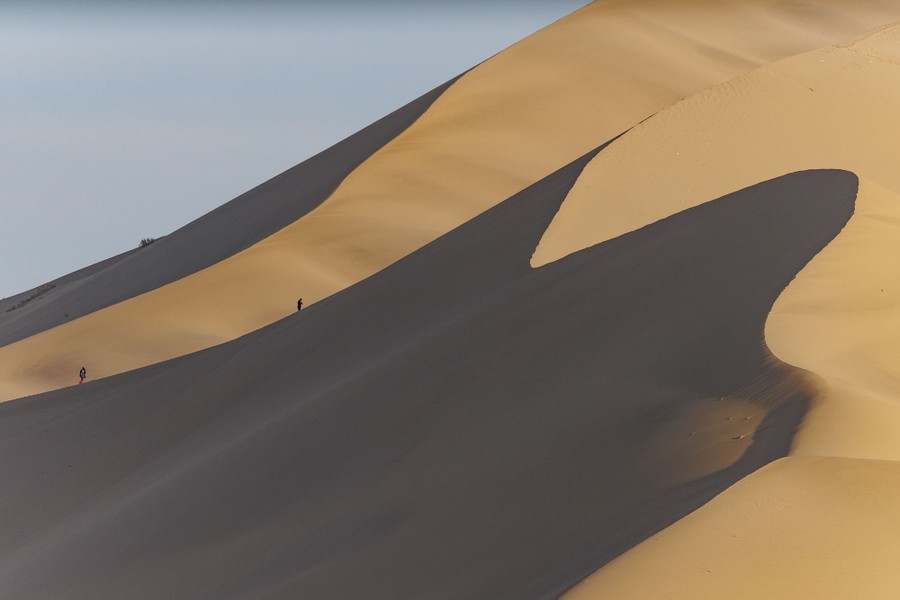 Several people walk along a very tall sand dune.