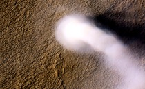 A white, billowy dust devil against the rust-colored, bumpy backdrop of Mars