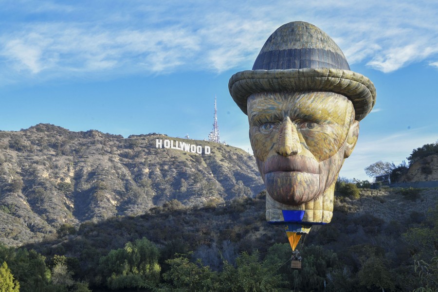 A hot air balloon shaped like the head of Vincent Van Gogh flies in front of the "Hollywood" sign in Los Angeles.