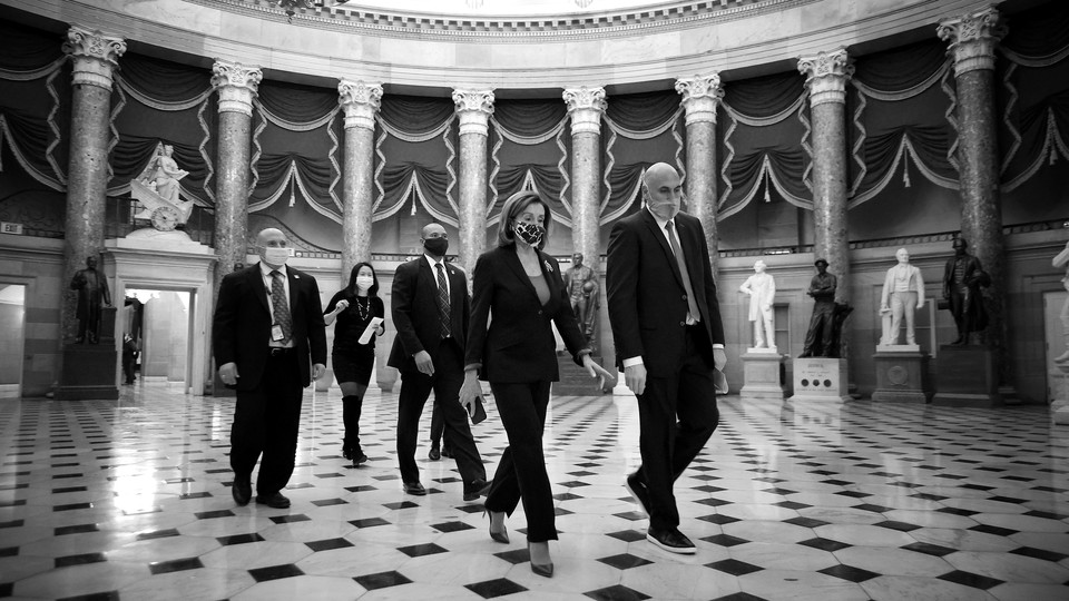 House Speaker Nancy Pelosi, surrounded by aides and security, walks through the Capitol rotunda.