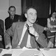 A black-and-white photograph of J. Robert Oppenheimer testifying before the Senate Military Affairs Committee in 1945.