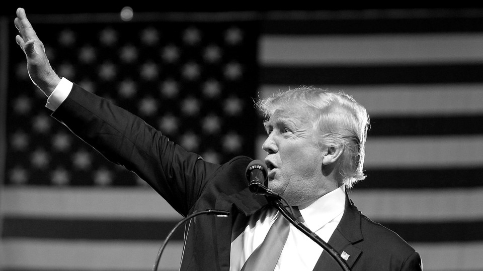 A black-and-white photo of President Donald Trump shows him waving as he stands behind a podium.