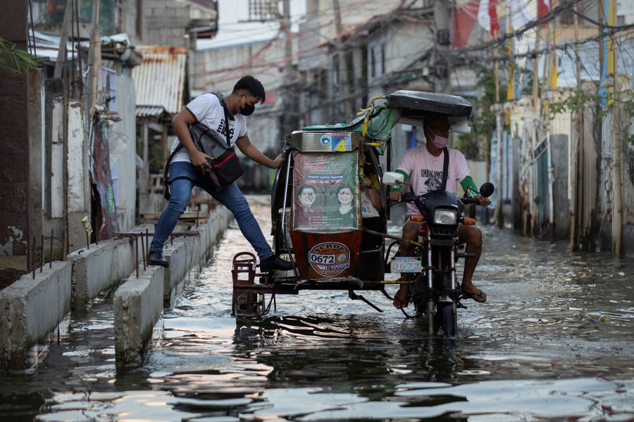 A person steps carefully into a motorcycle taxi in a flooded street.