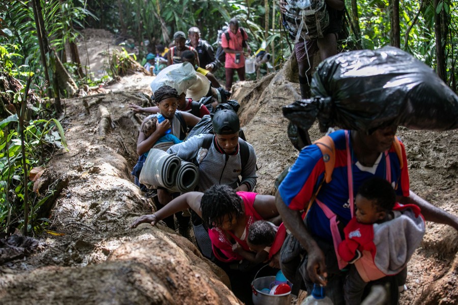 A group of migrants walks a muddy path through a jungle.