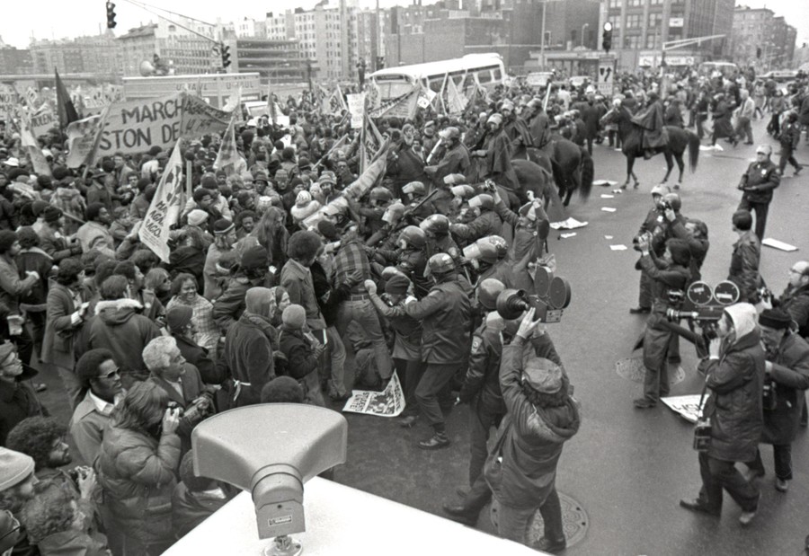 Riot police push up against a crowd of protesters in a city street.
