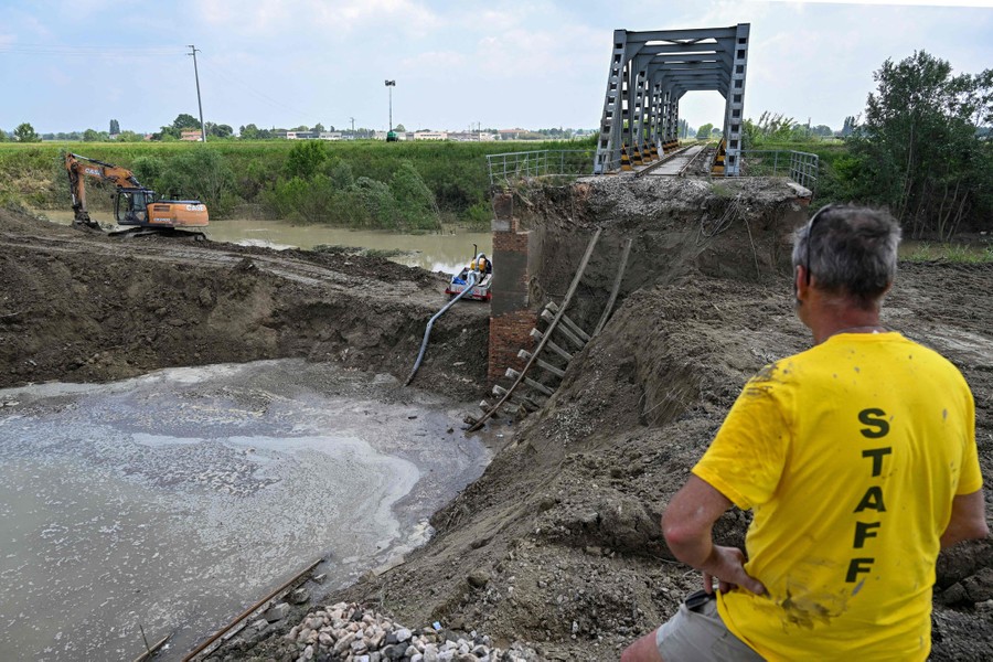 A person stands beside a heavily damaged railway bridge, following a flood.