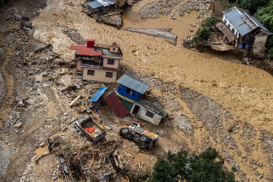 An aerial view of a riverbed after a heavy flood, with houses and vehicles strewn about