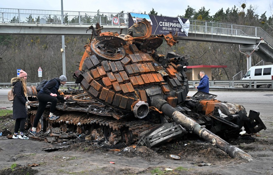 Several civilians take a close look at a destroyed military tank on a roadside.
