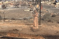 A statue stands in a backyard, amidst the rumble of a destroyed home. 