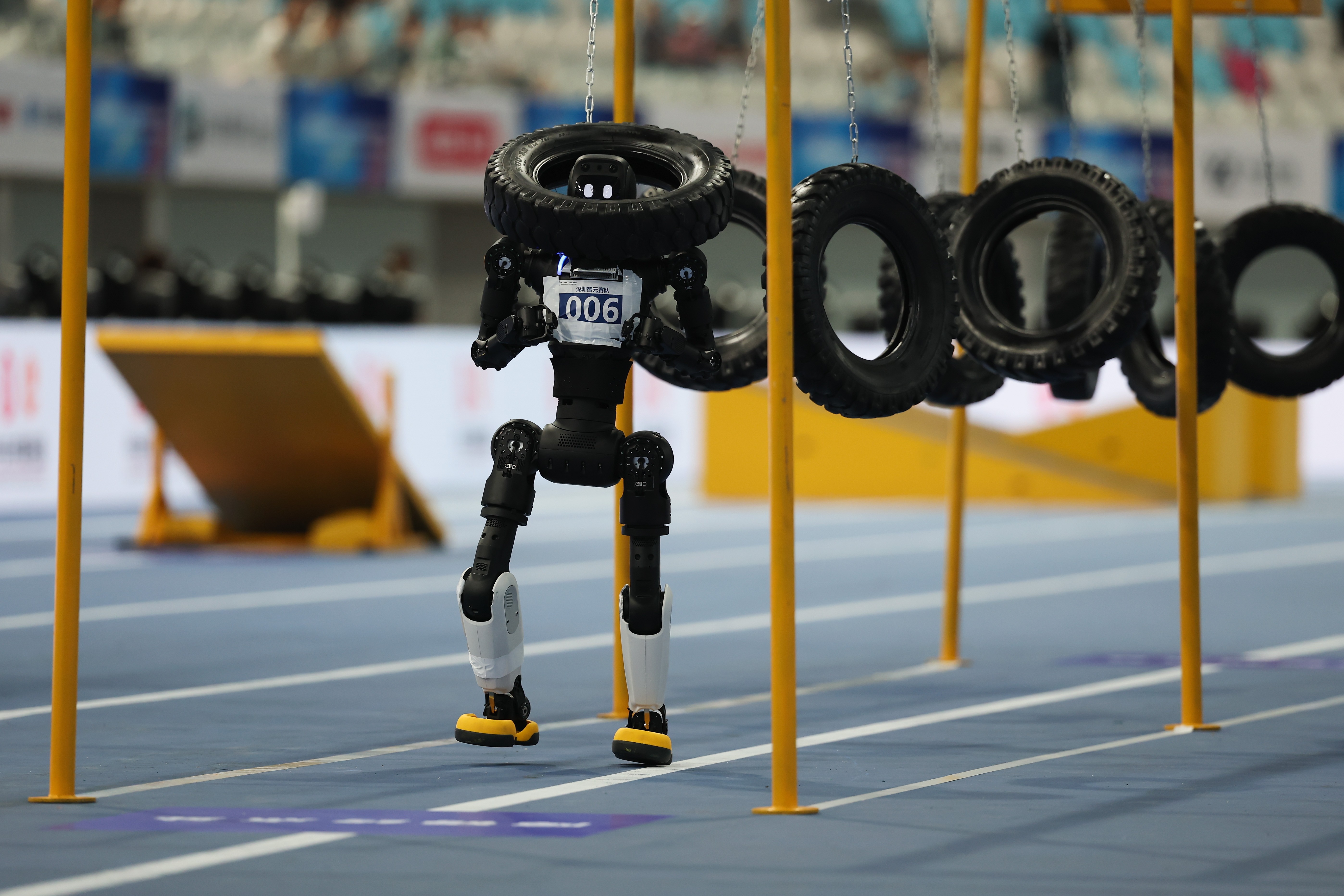 A humanoid robot is tangled in a swinging-tire obstacle during a race.