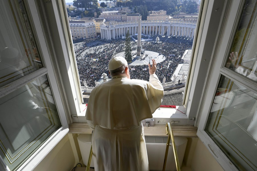 Captured from behind, Pope Francis waves from a window to a crowd gathered in St. Peter's Square below.