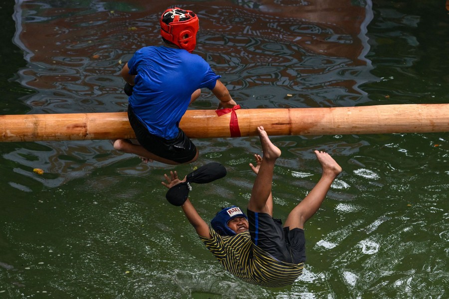 One child falls from a pole into water after being knocked off by another child, who is about to fall.