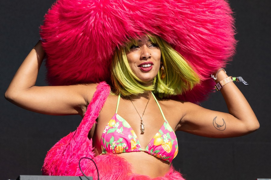 A person performs on stage, wearing a giant, fuzzy pink hat.