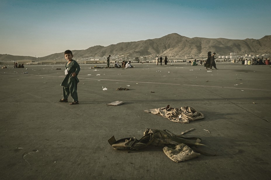 A child stands in an empty airfield with military jackets on the ground