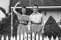 Two people waving over a white picket fence
