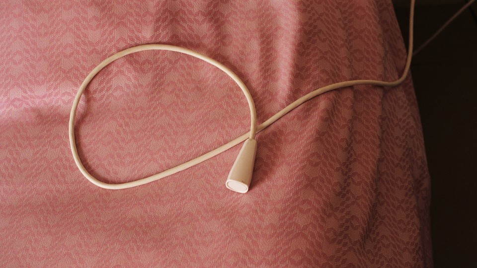 A hospital-assistance pull-cord rests on a pink bedspread on a hospital bed.