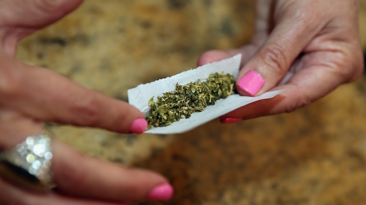 A woman's hands, with pink fingernail polish, holding a marijuana cigarette
