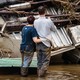 Two people stand in floodwater before wreckage in western North Carolina