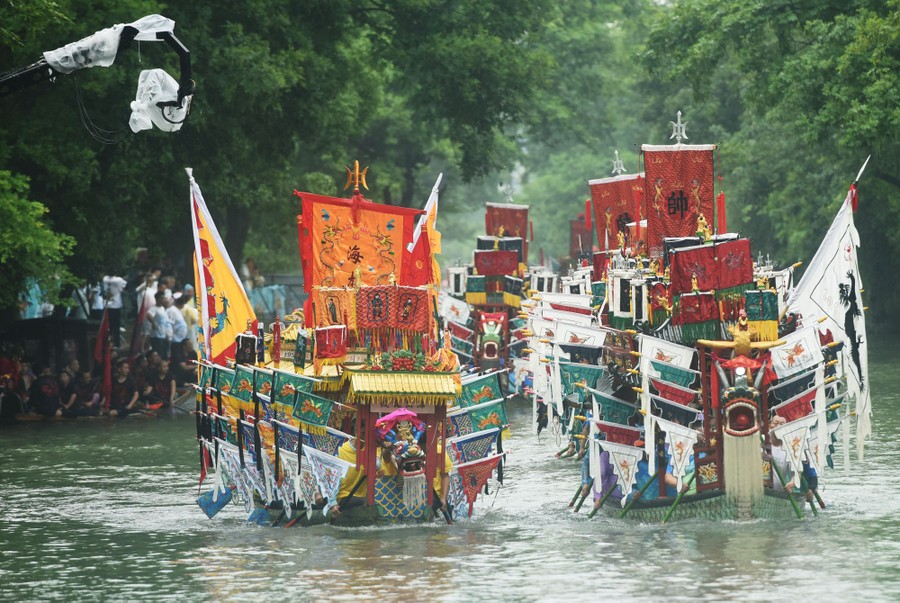 Dragon boats decorated in many flags pass by in a parade.