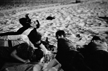 A group of young people lying on the beach, drinking in the sand at night