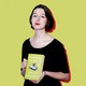 Sally Rooney poses with a copy of her book "Normal People" against a yellow background.