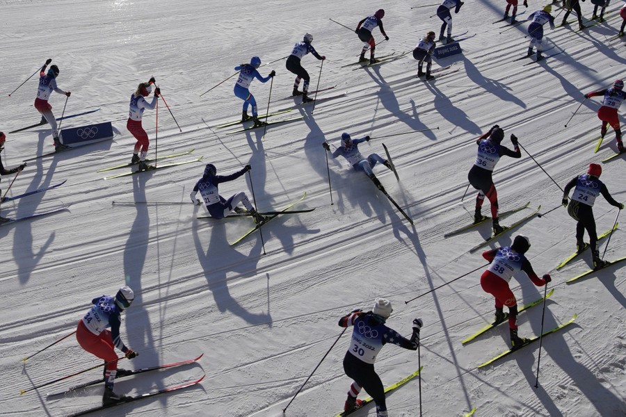 Two skiers among a pack of many others fall during a race.