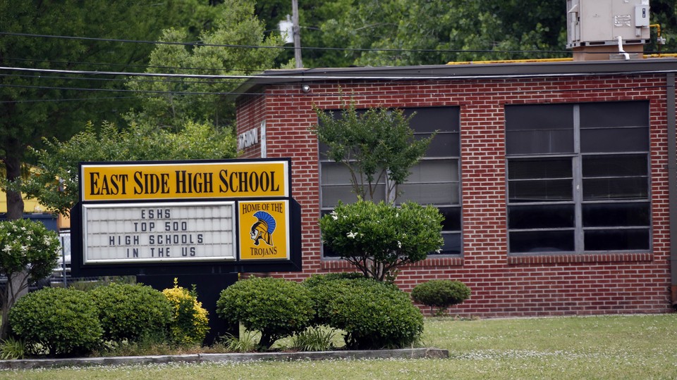 A sign reading "East Side High School: Top 500 High Schools in the U.S." sits outside a brick school building.