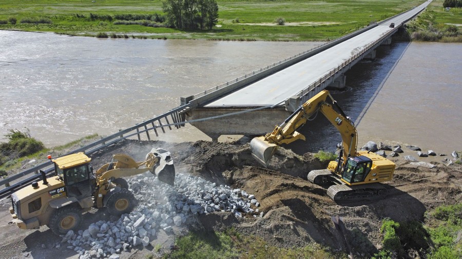 People use construction equipment to build up a river bank beside a washed-out bridge.