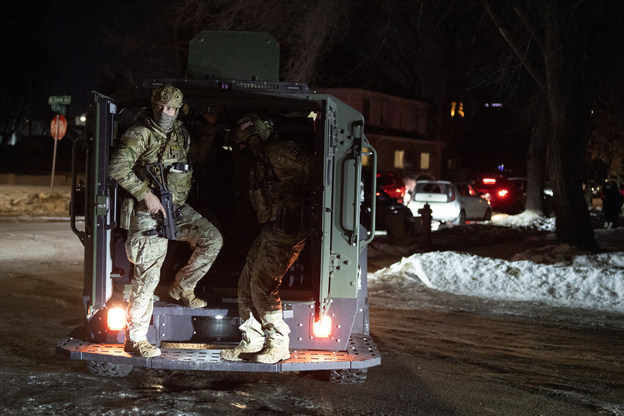 Masked and armed federal immigration officers in a vehicle at night with snow and ice on the street