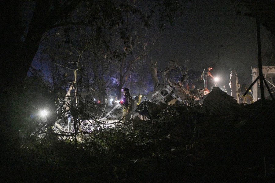 Emergency-service workers search through ragged piles of rubble and smashed trees at night.