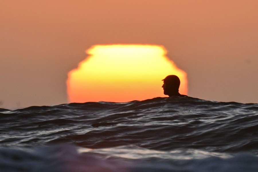 The head of a surfer above waves, with the setting sun in the background