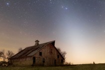 A photograph of an abandoned farm in rural Illinois at night, with the glow of zodiacal light overhead