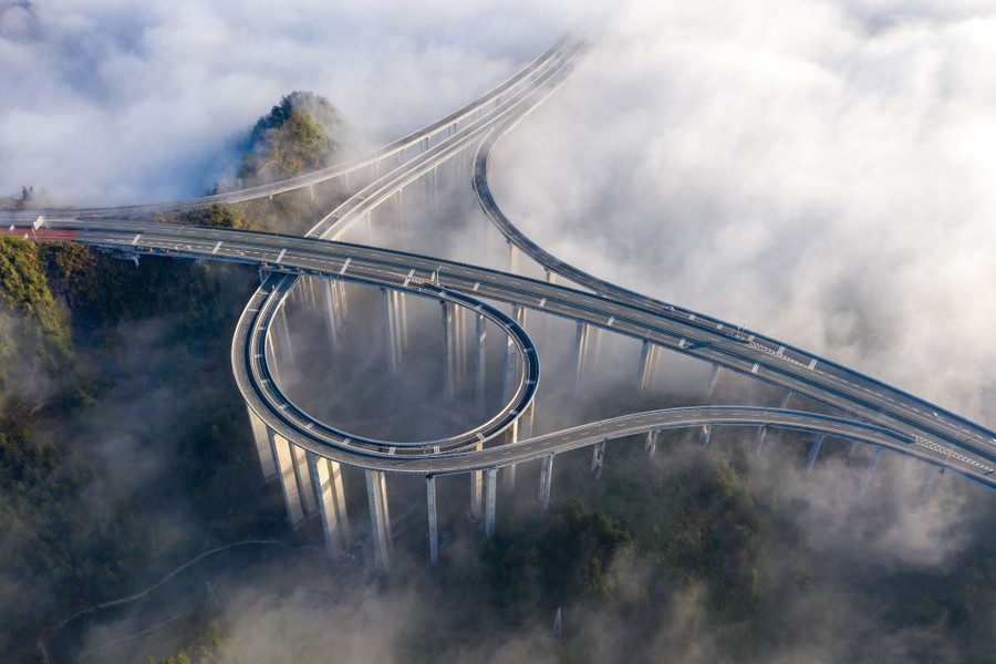 Low clouds cover the hilly landscape below an elevated, looping highway interchange.